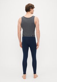 Γκρι αμάνικο μπ λουζάκι και ναυτικές κολάν, με μαύρη ζώνη που έχει κείμενο. Λείο ύφασμα, εφαρμοστή σχεδίαση. Θέα από πίσω.