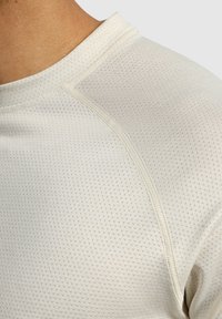 Ljust färgad träningströja med en texturerad tyg som har små diamantmönster, rund halsringning och förstärkta sömmar.