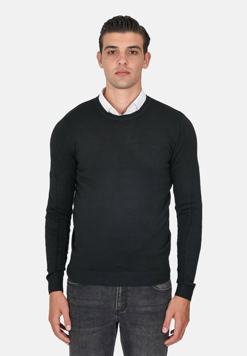 Maglione nero a maniche lunghe con scollo rotondo, realizzato in un tessuto a maglia liscia, con polsini e orlo a coste, indossato sopra una camicia bianca con colletto.