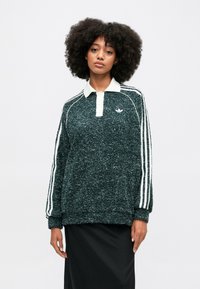 Sweatshirt de malha verde escuro com colarinho branco, três riscas brancas verticais nas mangas e pequeno logótipo no peito. Corte solto.