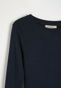 Granatowa, prążkowana bluzka z długim rękawem i okrągłym dekoltem. Materiał wydaje się miękki; etykieta widoczna wewnątrz obszaru dekoltu wskazuje rozmiar mały.