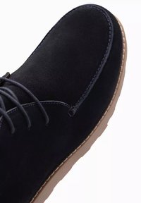 Chaussure décontractée en daim noir avec un bout arrondi, un design à lacets, une semelle en caoutchouc beige, et des accents brodés le long du bord.