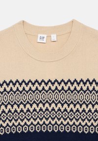 Beige strikkegenser med rund hals som har et marineblått geometrisk mønster over den nedre halvdelen. Lapper indikerer størrelse L og merke GAP Kids.