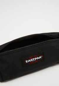 Astuccio nero in tessuto resistente, con chiusura a zip, forma rettangolare e un’etichetta logo Eastpak rossa e bianca sul davanti.