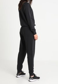 Svart fleece-tröja och joggingsbyxor, åtsittande design, elastiska muddar och midja, tillsammans med svarta träningsskor med vit sula.