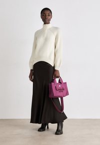 Knit cream sweater with high collar, black long skirt, and purple Coach bag featuring embroidered text, worn with black heeled boots.