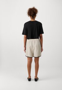 Tricou negru scurt cu mâneci scurte, asortat cu pantaloni scurți bej dintr-un material texturat, cu un tiv negru în formă de valuri. Pantofi slip-on negri.