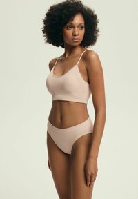 Miękki beżowy zestaw biustonosza i bikini wykonany z elastycznego materiału, z cienkimi regulowanymi ramiączkami i bezszwowymi wykończeniami dla maksymalnego komfortu.