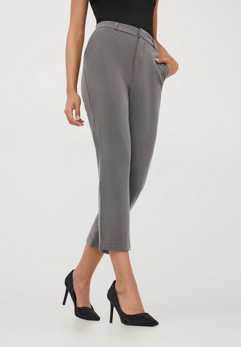 Pantaloni grigi su misura con design a gamba dritta, dotati di tasche laterali e una finitura impeccabile, abbinati a décolleté nere decorate.