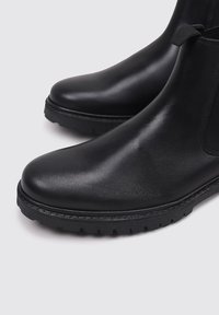 Botas de cuero negro hasta el tobillo con un acabado suave, paneles laterales elásticos y suela texturada resistente. Presentan una puntera redondeada y una construcción sólida.