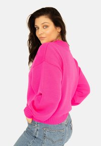 Różowy sweter z dzianiny z prążkowanym dekoltem okrągłym, w luźnym kroju i bufiastymi rękawami. Połączony z niebieskimi dżinsami z wysokim stanem, prezentując swobodny look.