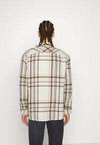 Camicia a maniche lunghe a quadri in crema con linee marroni e beige, caratterizzata da una vestibilità comoda, polsini con bottoni e un giogo sul retro.