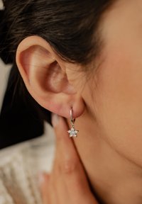 Boucles d'oreilles en argent en forme de créoles ornées d'un design étoilé agrémenté de pierres précieuses transparentes. Les boucles d'oreilles pendent du lobe de l'oreille, mettant en valeur les détails et l'éclat.