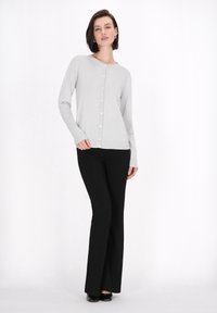 Cardigan grigio chiaro abbottonato con maniche lunghe, abbinato a pantaloni neri a palazzo e scarpe nere. Texture liscia e design aderente.