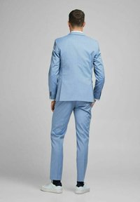 Ljusblå kostym med skräddarsydd passform, med slagkrage och sidofickor. Bärs med vita sneakers och marinblå strumpor.