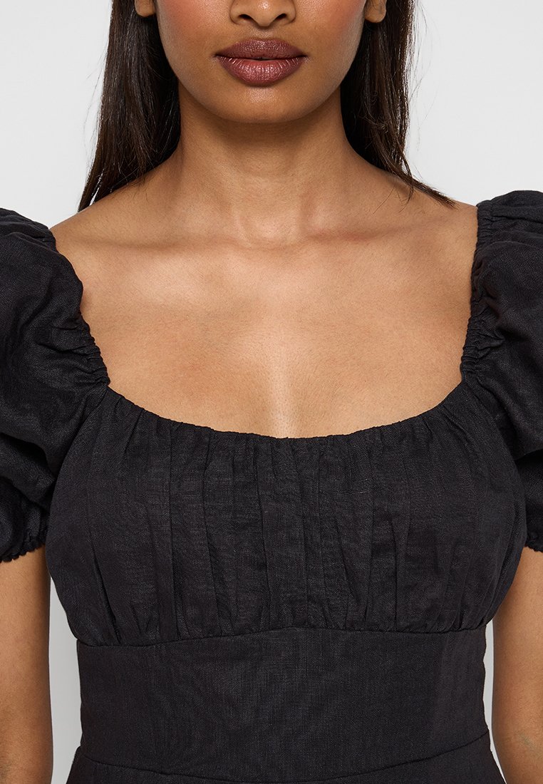 Robe noire à manches bouffantes avec un décolleté carré, présentant un tissu texturé et des détails froncés sur les manches et le buste.