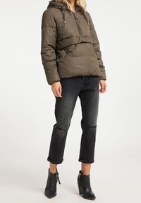 Giacca puffer verde oliva con cappuccio, zip frontale a metà, polsini elasticizzati e cuciture orizzontali. Abbinata a jeans neri con effetti usurati e stivaletti.