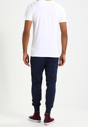 Wit T-shirt met korte mouwen en marineblauwe joggingbroek met elastische boorden en minimalistisch ontwerp, gecombineerd met bordeauxrode hoge sneakers.