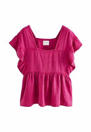 Femme portant un haut fuchsia ample et texturé avec des manches volantées et un short assorti à cordon, posant devant un fond neutre.