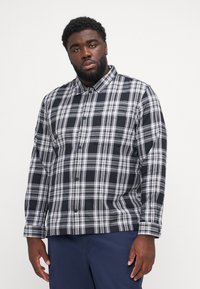 Black and white checked shirt with a button-down collar, long sleeves, and a single chest pocket, made of smooth fabric.