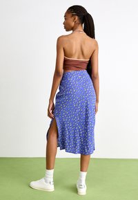 Fustă florală albastră cu fante laterale, realizată dintr-un material ușor. Top scurt maro cu un design halter. Tenisi albi cu accente argintii.
