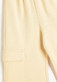 Beige joggers i mjukt material, med en sidficka med klaff och ett bekvämt elastiskt midjeband. Slät textur och avslappnad passform.