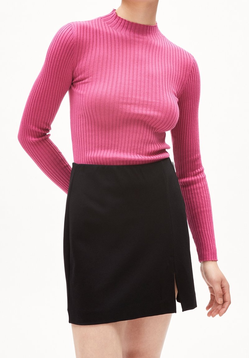 En figurnära ribbad rosa långärmad topp matchad med en svart minikjol med en slits på sidan; båda plaggen har en slät textur och en elegant design.