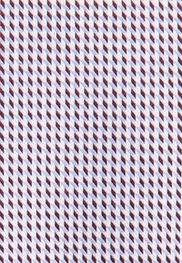 Tessuto caratterizzato da un motivo geometrico di zig-zag alternati rosso-marrone e blu chiaro su uno sfondo crema; texture liscia.