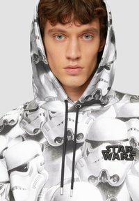 Bluza z kapturem z wzorem hełmów Stormtrooperów w czerni i bieli, z czarnym logo "STAR WARS" z przodu.