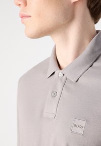 Gray polo shirt with a fold-over collar, two buttons, and embroidered logo patch on the chest. Soft, textured fabric.