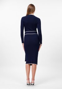 Tummansininen ribbimäinen midi-mekko, jossa on pitkät hihat ja valkoiset yksityiskohdat vyötäröllä ja hihoissa. Suunniteltu slim fit -malliseksi ja siinä on sivuaukot.