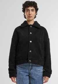 Zwarte sherpa-jack met een kraag, knopen aan de voorkant, zijzakken en een cropped ontwerp. Zachte textuur en ontspannen pasvorm.