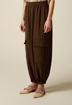 Persona che indossa pantaloni cargo marroni larghi con polsini elastici abbinati a ballerine beige con lacci intrecciati.