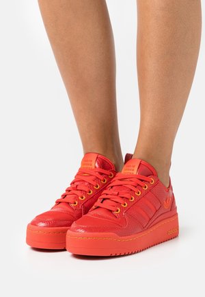 Zapatillas rojas con un upper de cuero texturizado, suela de goma lisa y ojales amarillos. Presenta una lengüeta acolchada y un sutil detalle de logotipo.