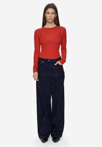 Rød langærmet top kombineret med mørkeblå vide bukser med høj talje og sidelommer. Elegante sorte sko fuldender looket.
