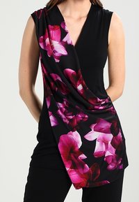 Black top with a deep V-neck, featuring a draped design adorned with large pink floral patterns on one side. Soft fabric with a flowing texture.