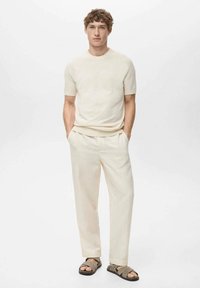 Cream-colored knitted short-sleeve top, loose-fitting cream trousers, and brown slide sandals. Smooth texture with a minimalist design.