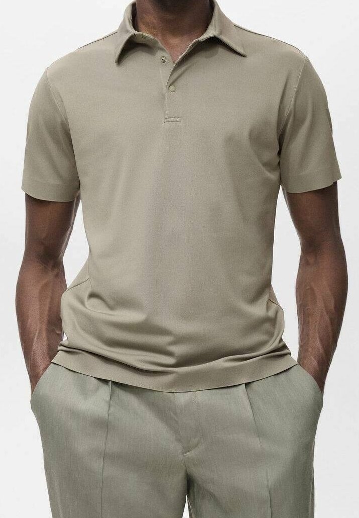 Homme portant un polo beige à manches courtes et un pantalon gris clair, les mains dans les poches, sur un fond uni.