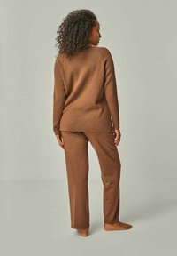Braunes gestricktes Loungewear-Set, bestehend aus einem Langarmshirt und passenden Hosen. Der Stoff hat eine weiche Textur und einen lockeren Sitz.