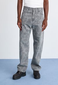 Grå camo-mønstret jeans med løs passform, med knapp- og glidelås-lukking, og brukt med svarte snørestøvler.