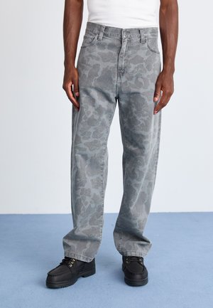 Gray camo-patterned jeans with a loose fit, featuring a button and zipper closure, and worn with black lace-up shoes.