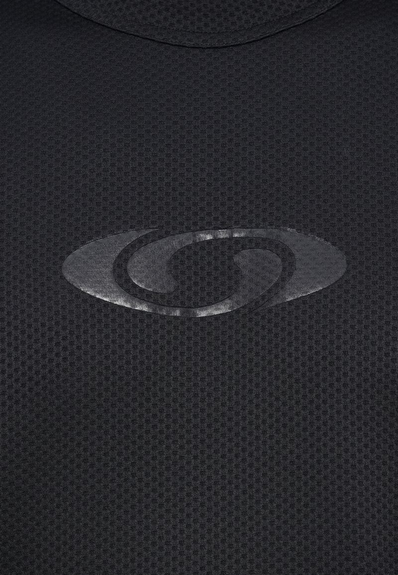 Tessuto nero con texture e un pattern sottile. Presenta un logo lucido mostrato in maniera prominente al centro. Materiale liscio e traspirante.