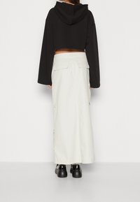 Sweat à capuche noir court avec manches larges, associé à une longue jupe blanche structurée avec poches latérales, et des chaussures à plateforme noires.