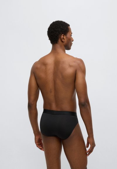 Zwarte slips met een brede elastische tailleband, aansluitend ontwerp dat de achterkant omhult, gemaakt van gladde stof, met minimale zichtbare naden.