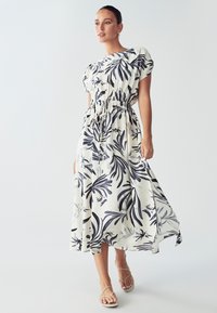 Maxi obleka iz lahkega materiala, z belo podlago in mornarsko modrim tropskim listnatim vzorcem, kratkimi napihnjenimi rokavi in nastavljivim vrvico v pasu.