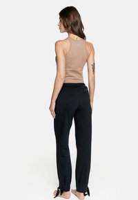 Beżowy top bez rękawów w zestawieniu z czarnymi spodniami dresowymi. Spodnie mają elastyczny pasek w talii i wiązania przy kostkach. Gładka tekstura materiału.