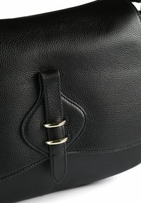 Zwarte leren handtas met een gestructureerde afwerking, een gebogen bovenkant en een decoratieve riem met twee ringen in goudkleur.