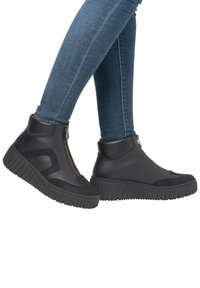 Bottines noires à zip, avec des accents texturés noirs et une semelle en caoutchouc épaisse et nervurée. Matériaux en cuir lisse et textile.