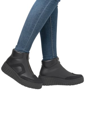 Black ankle boots with a zip closure, textured black accents, and a thick, ridged rubber sole. Smooth leather and textile materials.