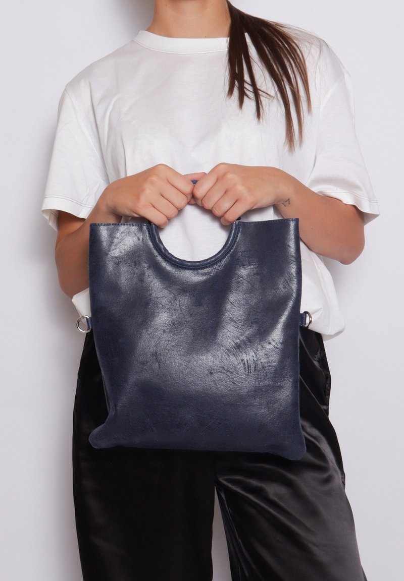 Navy leren totebag met een afgeronde handgreep en een gladde textuur. Heeft een minimalistisch ontwerp en een slank, rechthoekig formaat.